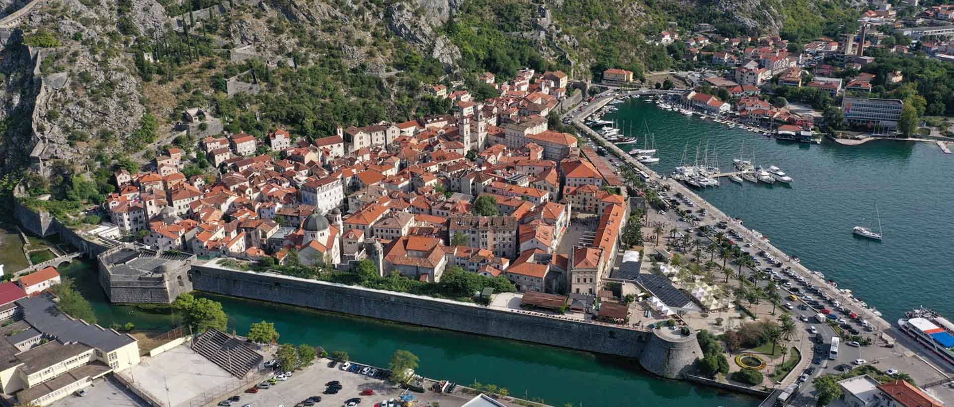 Drone view of Old Town Kotor, with Kotor marina and yachts inside it. Roofs of local houses are visible, inside this fortified town.